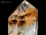 Quartz crystal with golden rutile needle inclusions and defined termination on dark background.