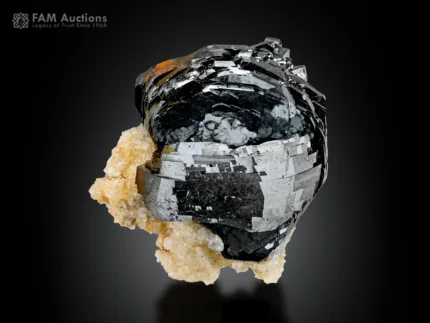 Lustrous hematite crystal cluster with layered metallic faces on pale matrix.