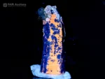 Blue afghanite crystal coated with lazurite and accented by pyrite, showing intense orange fluorescence under UV light.