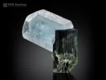 Aquamarine crystal resting on dark striated tourmaline specimen.