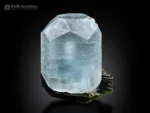 Aquamarine crystal resting on dark striated tourmaline specimen.