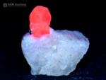 Pinkish-red ruby crystal on a white matrix with a pyrite accent and strong orange-red fluorescence under UV light.