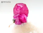 Pinkish-red ruby crystal on a white matrix with a pyrite accent and strong orange-red fluorescence under UV light.