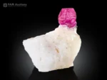 Pinkish-red ruby crystal on a white matrix with a pyrite accent and strong orange-red fluorescence under UV light.