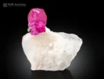 Pinkish-red ruby crystal on a white matrix with a pyrite accent and strong orange-red fluorescence under UV light.